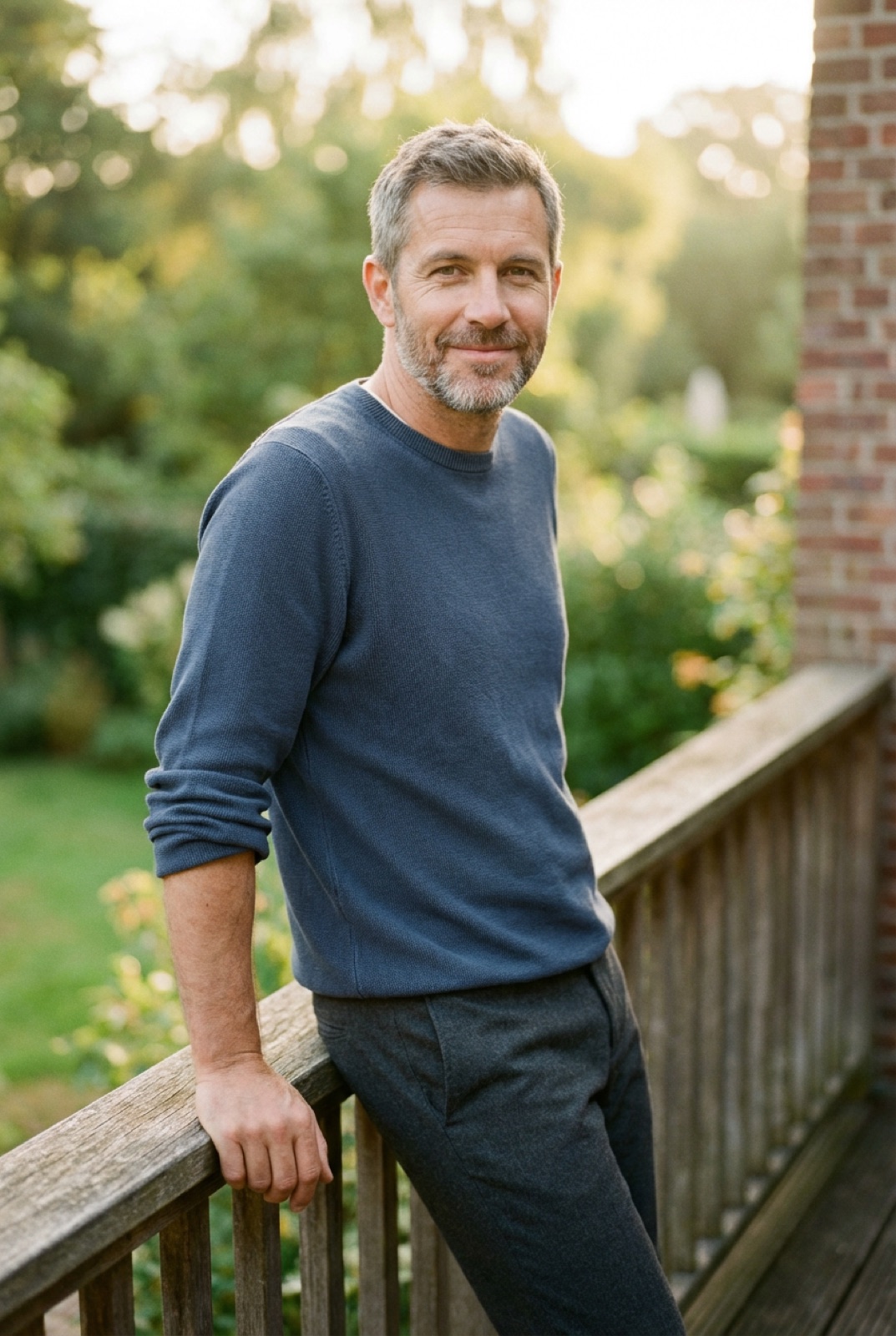 Confident man in his early 50s leaning on a wooden balcony railing, calm and grounded in morning light